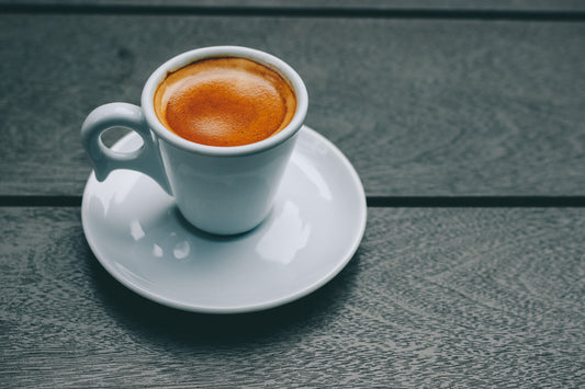 shot of espresso in a white, porcelain cup with a saucer witting on a wood background